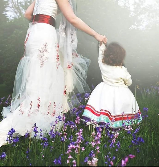 A lady and child wearing long white dresses walking through a meadow.