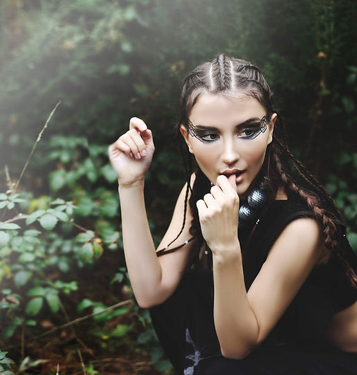 A girl with braided hair and a latex outfit posing in the woods.