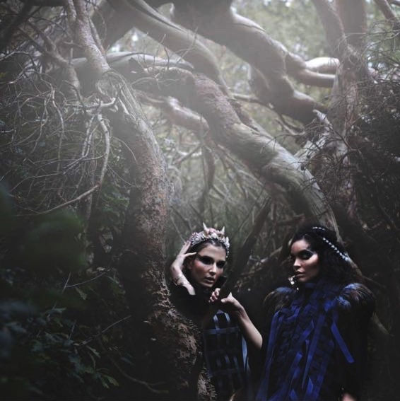 Two women wearing witch-like clothes in a misty forrest.